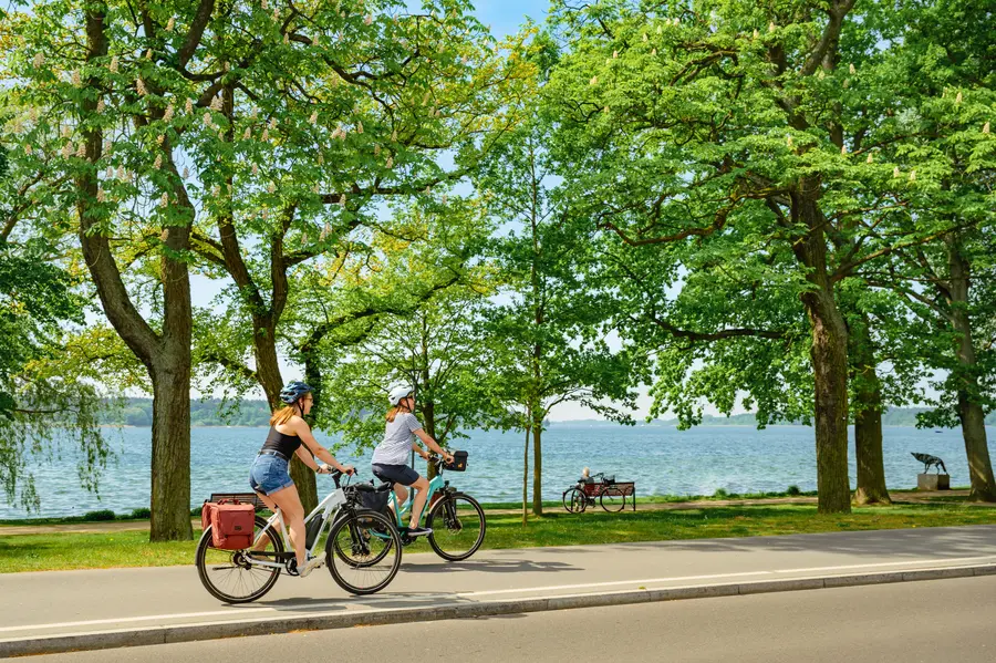 Mutter und Tochter fahren auf Rädern an einem See entlang.